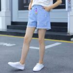 The Candy Button Ripped Shorts - Trendy light-blue distressed denim shorts featuring vibrant, colorful front buttons and frayed hems